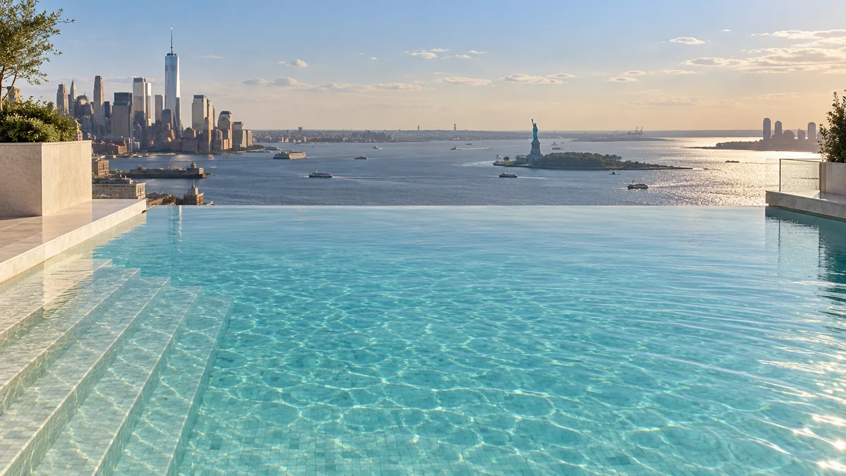 An imagined New York rooftop infinity pool looking across the harbor toward the Statue of Liberty.